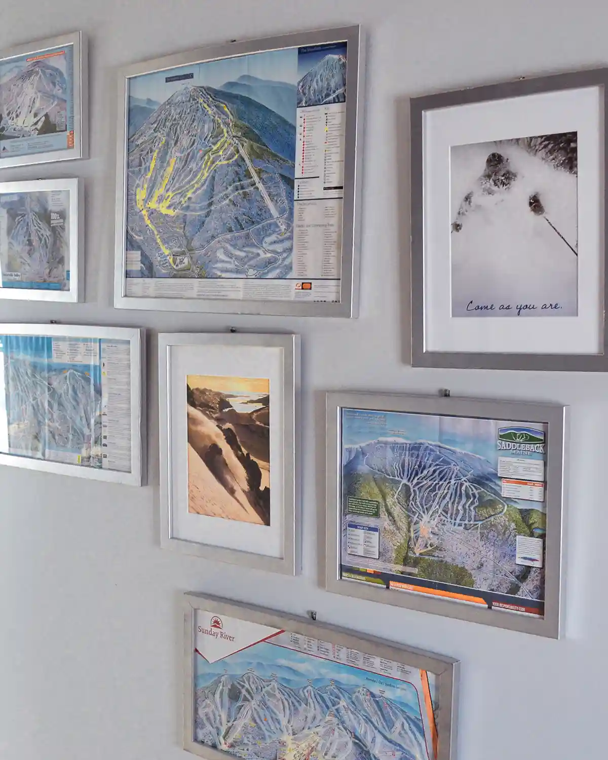 A collection of DIY framed ski maps in silver spray painted frames hangs in a hallway along with other skiing themed prints to form a ski themed gallery wall