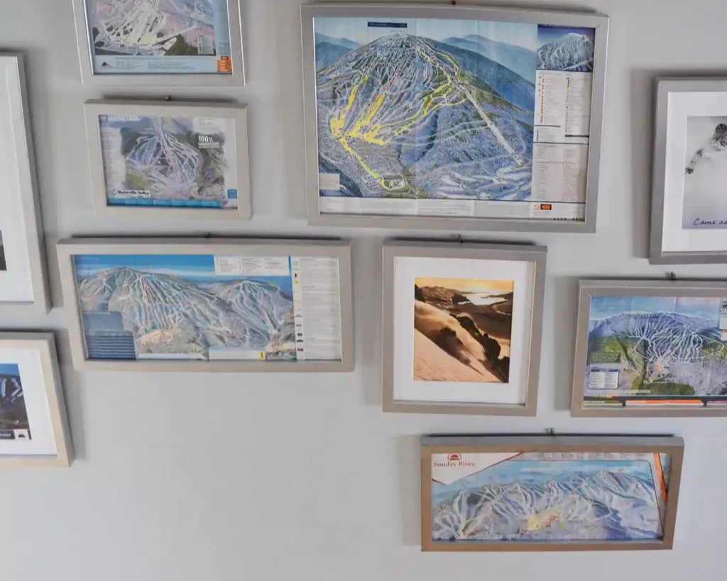 A collection of framed ski map art and prints from POWDER Magazine hanging in a ski themed gallery wall with simple silver frames