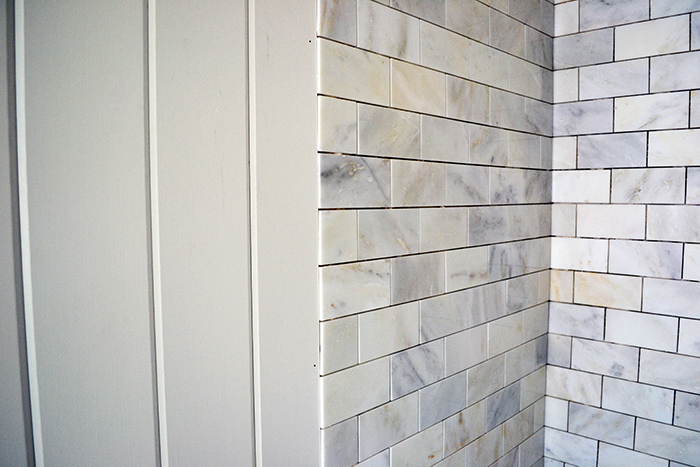 Combination of marble subway tiles in a shower and planked walls in a bathroom remodel