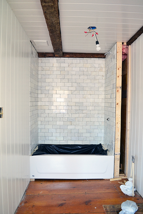 Installed marble subway tile in a guest bathroom shower combined with planked walls and rustic wood beams