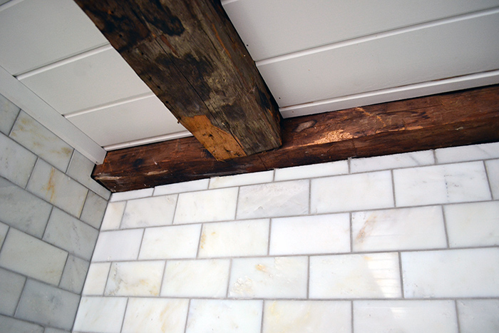 Bathroom renovation using marble subway tiles for a shower surround to complement old wood beams.