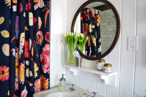 Bathroom renovation with white planked walls and ceiling, an Anthropologie shower curtain, and vintage mirror and sink.