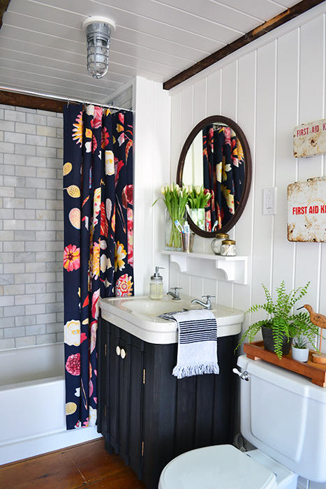 Guest bathroom renovation reveal including marble subway tile shower, repaired toilet, white planked walls and ceiling, and vintage first aid kits, mirror, and sink.