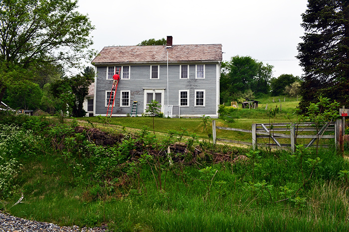 Scraping the exterior of an old colonial farmhouse to prepare it for painting