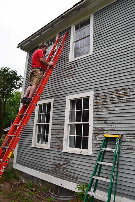 Scraping, repairing, and painting the clapboards of an old colonial farmhouse