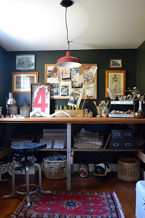 Dark craft room with a red farmhouse light fixture pendant above a rustic wood work bench