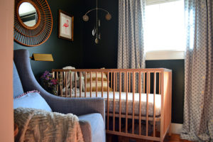 Baby girl nursery with dark walls, pink rug, Ikea crib, and West Elm Graham Glider
