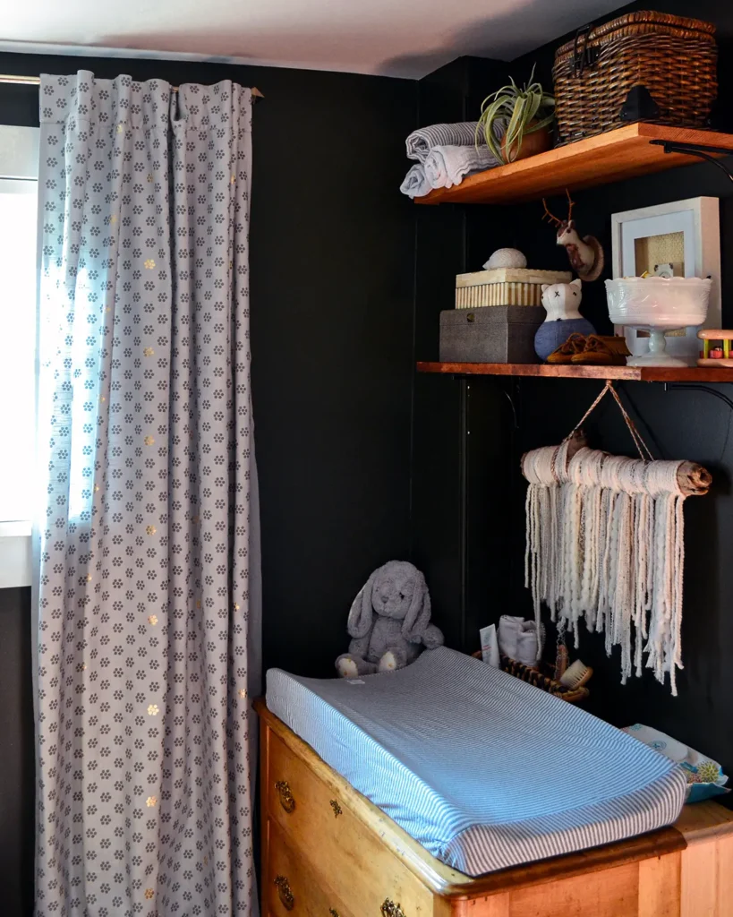 Open shelf styling in a moody nursery above a changing pad on a neutral toned vintage dresser