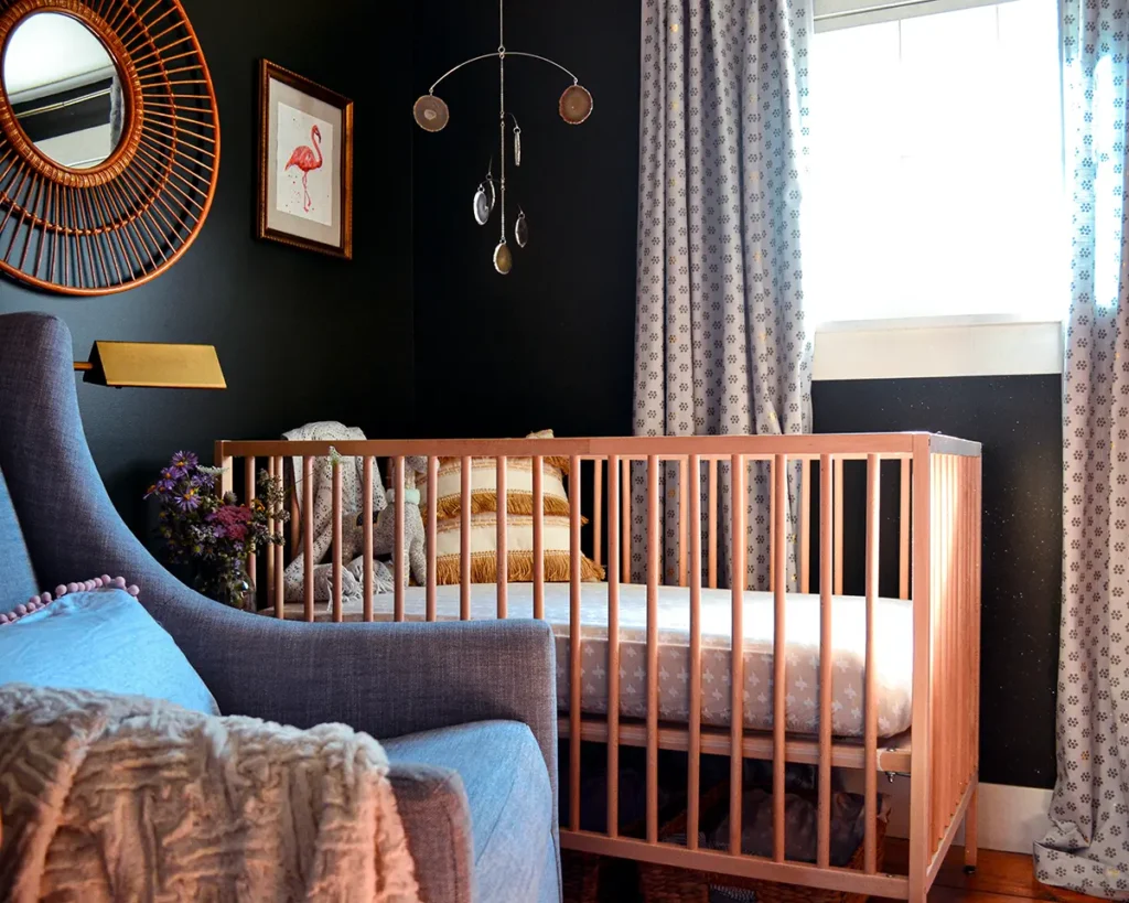 A moody nursery with an Ikea crib and a West Elm glider, black wall color contrasting with neutral furniture