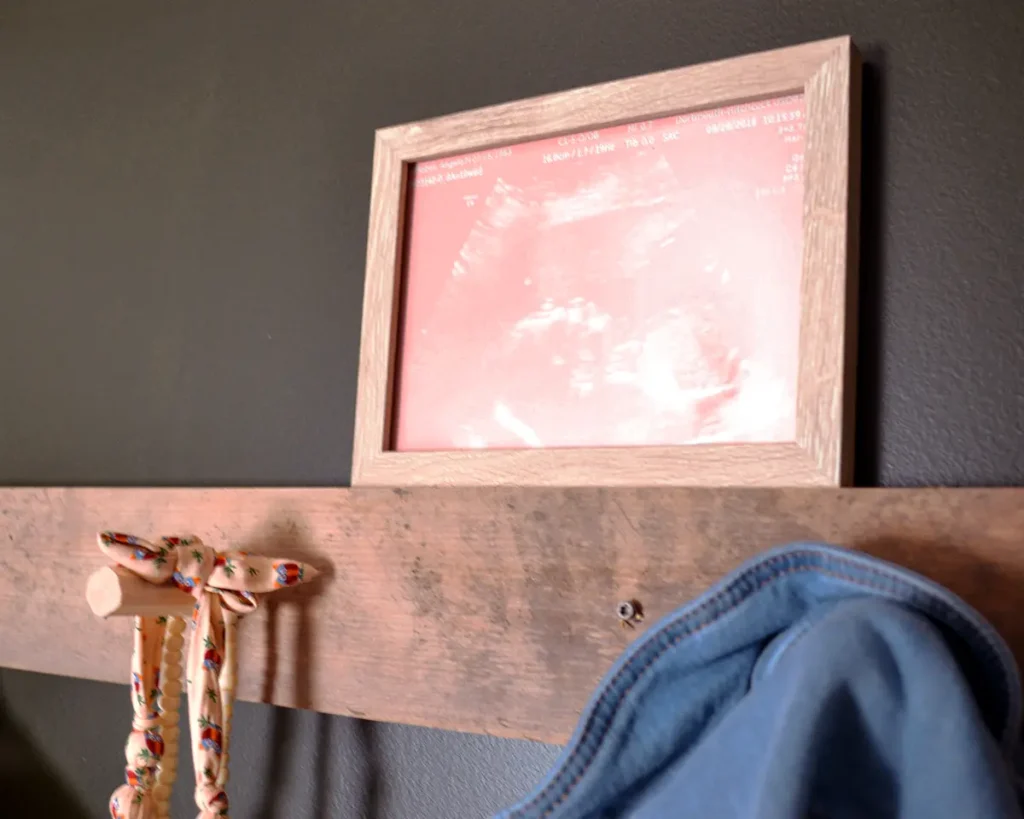 Pink ultrasound art print framed and hung above rustic pegs in a dark nursery