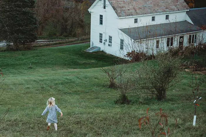 View of a 1700s Vermont farmhouse from the backyard with a child running down the hill