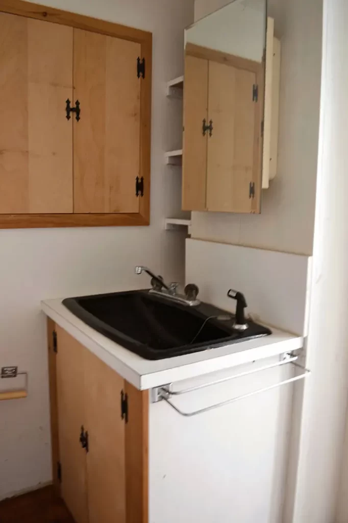 Small bathroom renovation vanity area with black sink and dated medicine cabinet