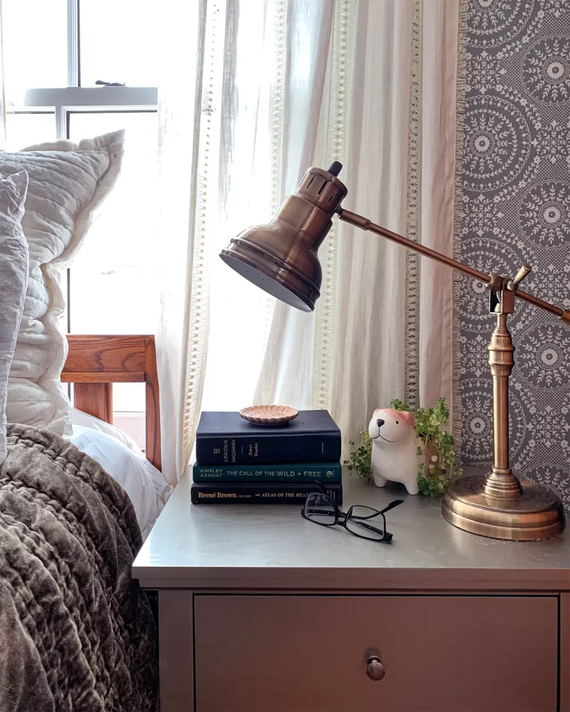 Bedroom nightstand styling with brass lamp, stack of books, and puppy planter