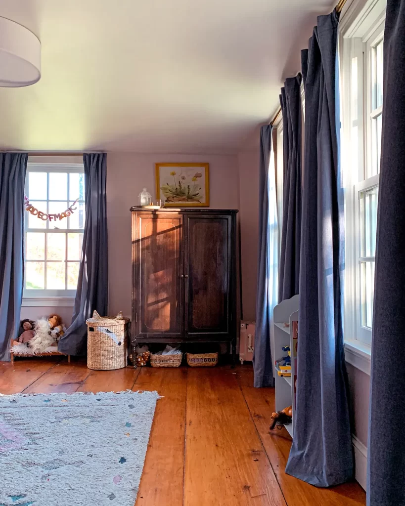 Kids bedroom with pink walls, chambray curtains and an antique wardrobe for clothes storage