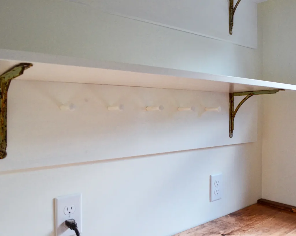 DIY laundry room shelves with a peg rail on the bottom shelf all painted white