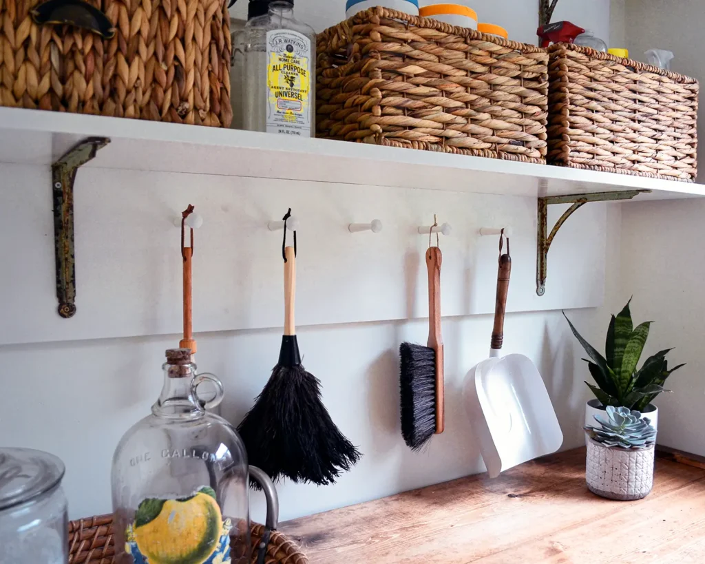 Swapping out dusters and dustpans for more stylish versions and hanging them from a peg rail in a small laundry room with open shelves for added storage