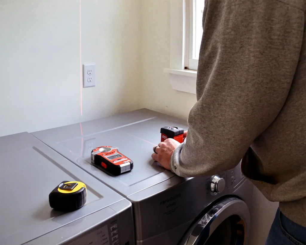 A laser level and a stud finder helps determine where to hang shelves above laundry machines