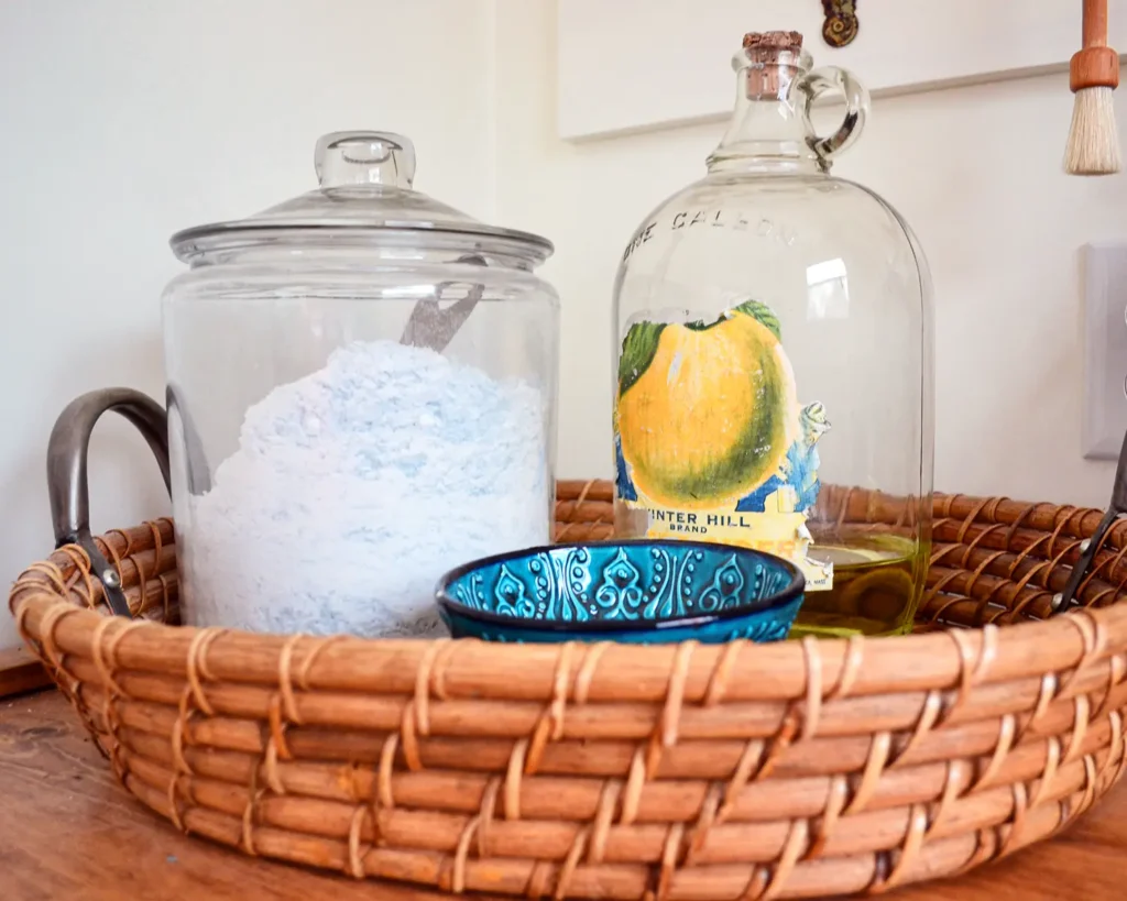 Decanting laundry powder detergent and bleach into glass jars, corralling in a woven tray, and placing on top of a laundry countertop