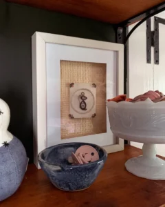 Baby accessories stored on a shelf, including pacifiers in a pottery bowl and hair bows in a vintage milk glass footed bowl