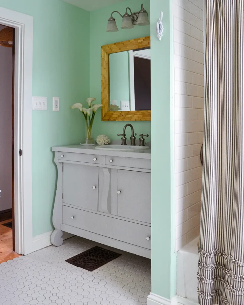 The after photo of a bathroom renovation with mint green walls, wood tiled mirror, and light gray buffet turned into a vanity