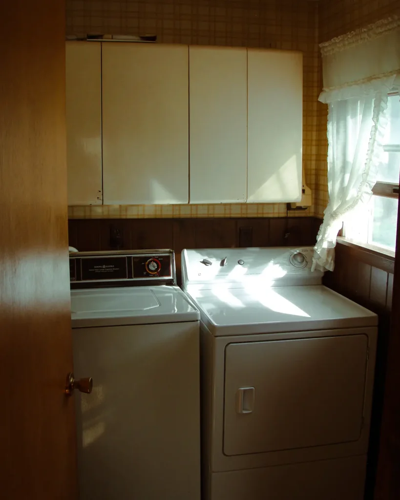 Before picture of the DIY laundry room makeover featuring old metal upper cabinets and plastic paneling