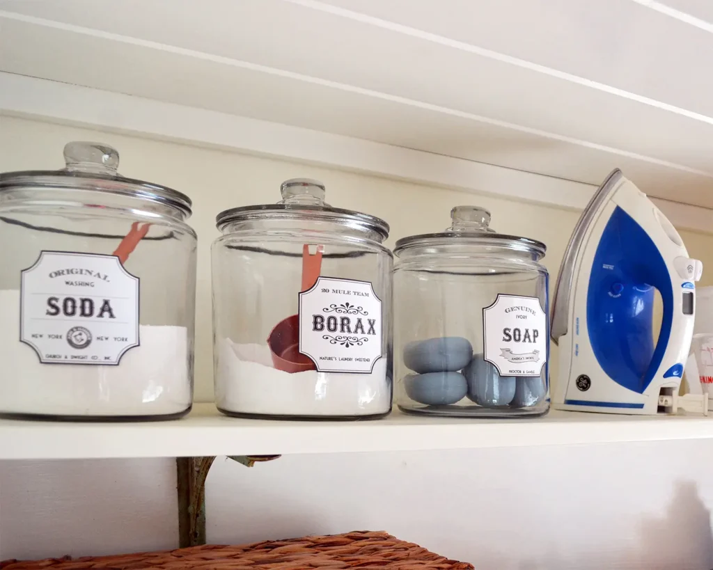 Glass jars for storing laundry detergent making supplies on the top shelf of the laundry room shelves