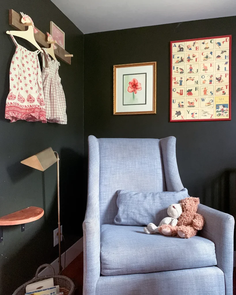 A small nursery with dark walls and special baby dresses hanging from a peg rail