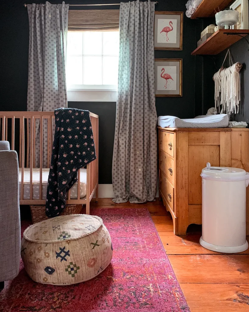 A baby girl's nursery with dark painted walls, bright pink rub, light wood toned furniture