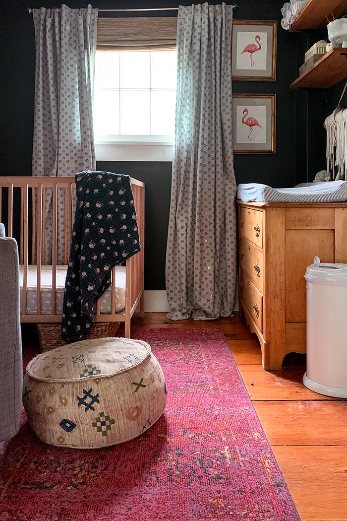 A small nursery in a Vermont farmhouse featuring wide pine floors, dark green walls that are almost black, vintage storage finds, and a simple Ikea crib
