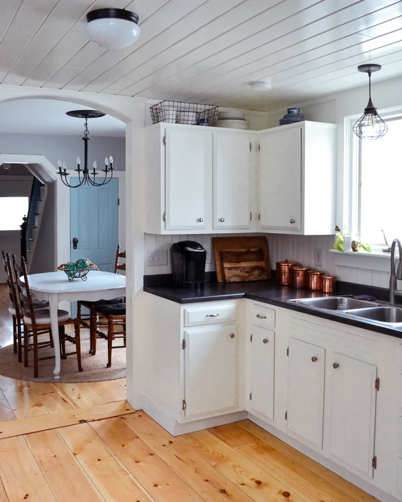 Kitchen renovation after picture with white painted cabinets, wide pine floorboards, and a shiplap ceiling