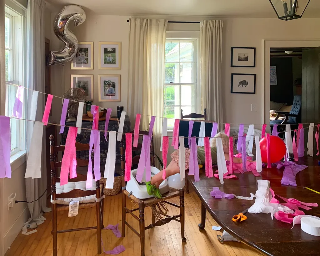 Assembling the DIY crepe paper bunting by hanging the string among windows and chairs, hanging streamers, and stapling to the jute