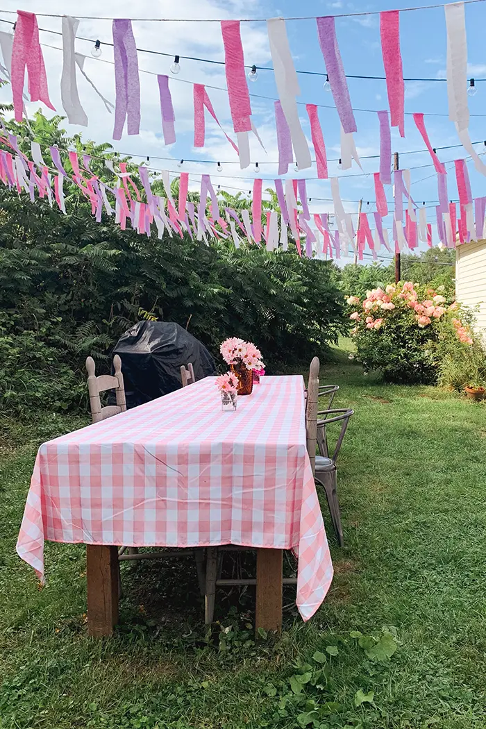 DIY crepe paper bunting made with streamers hanging above an outdoor dining table for a little girl's second birthday party