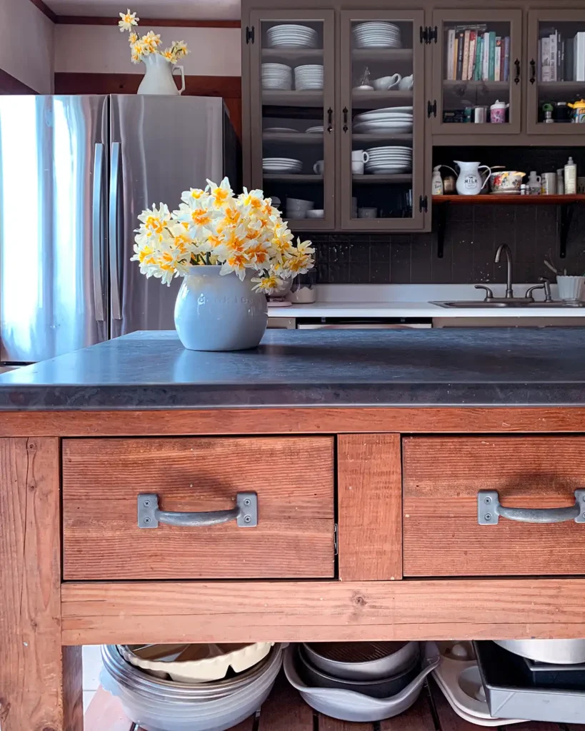 Kitchen island finished with a wood stain and matte finish with a laminate counter top and dark green kitchen cabinets behind it