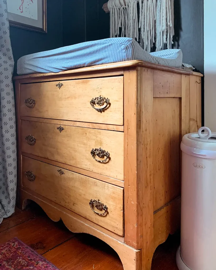 Vintage natural wood dresser showing patina and age in a nursery with dark walls