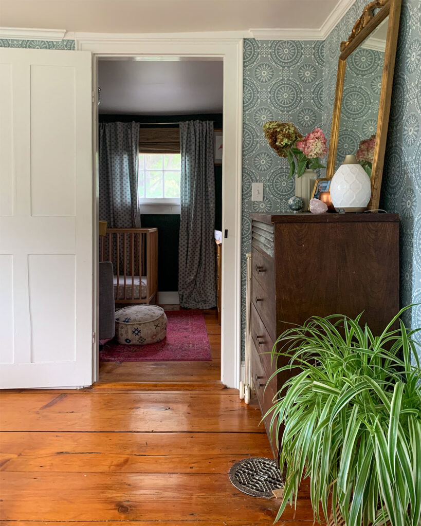 A master bedroom looking to the nursery space in the master bedroom showcasing wide pine floorboards, spider plant and vintage dresser