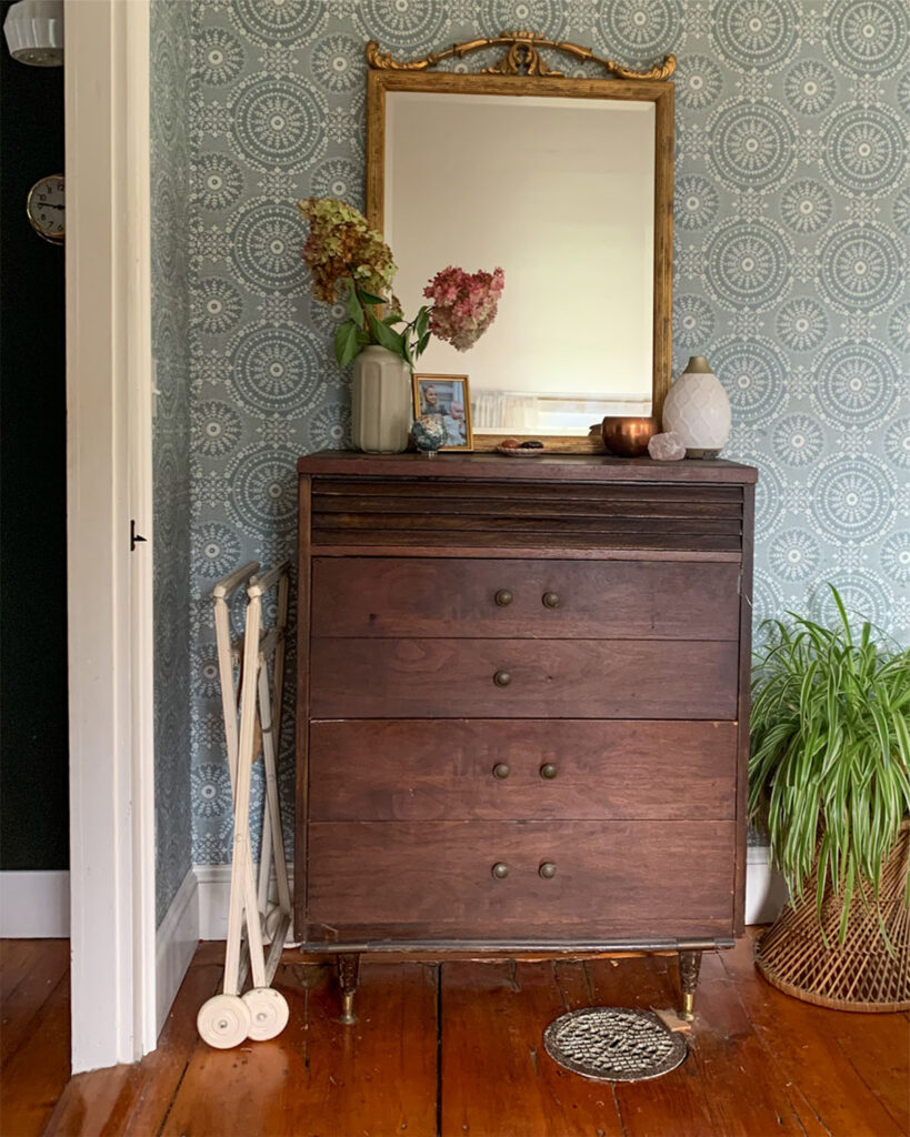 A vintage dresser combined with a vintage mirror with a plant and simple styling on the top of the dresser