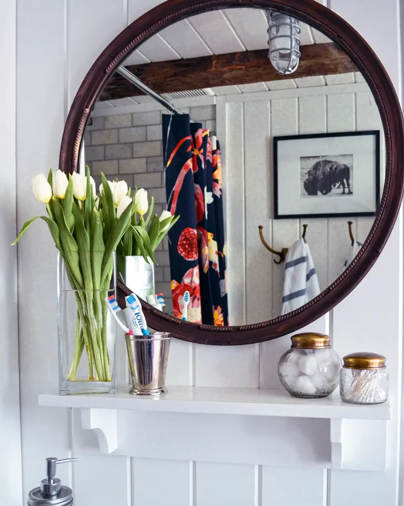 Final touches in a bathroom project with vintage mirror, apothecary jars, flowers, and julep cup for toothbrushes