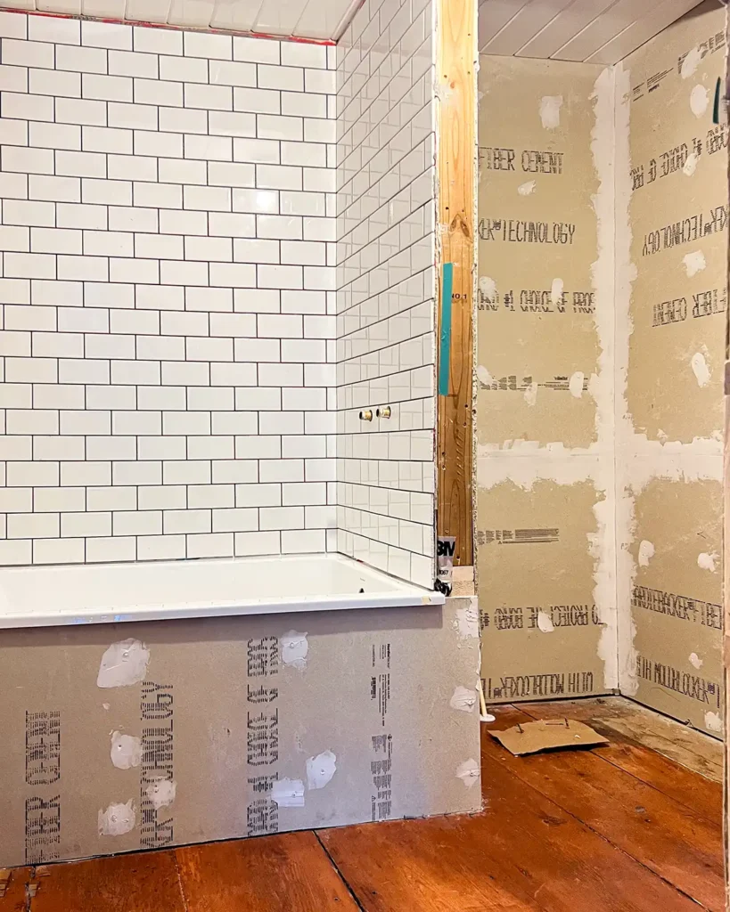 Small bathroom renovation progress with white subway tile installed around a shower and cement board where tile will go