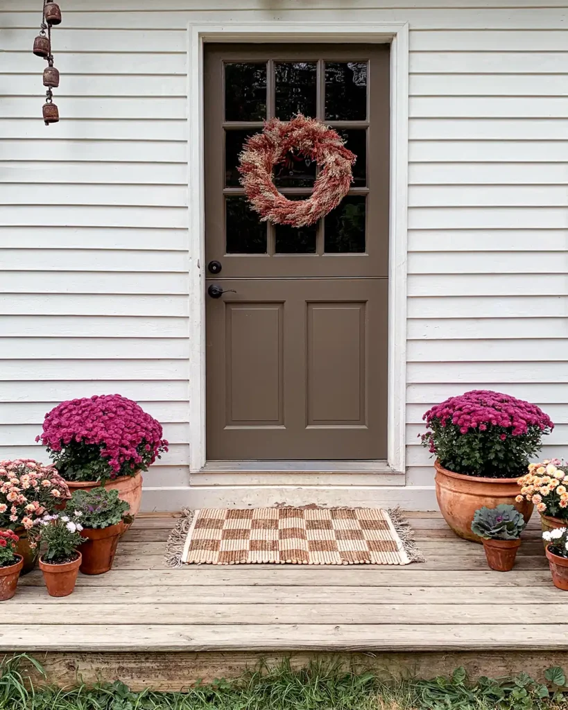 Flower pots on a front porch of different heights filled with mums and ornamental kale