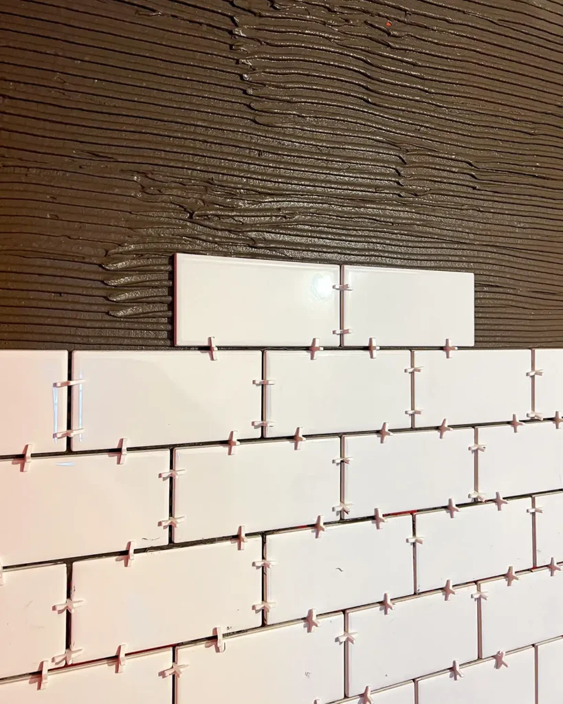 Installing white ceramic subway tile around a shower with dark grey thinset mortar