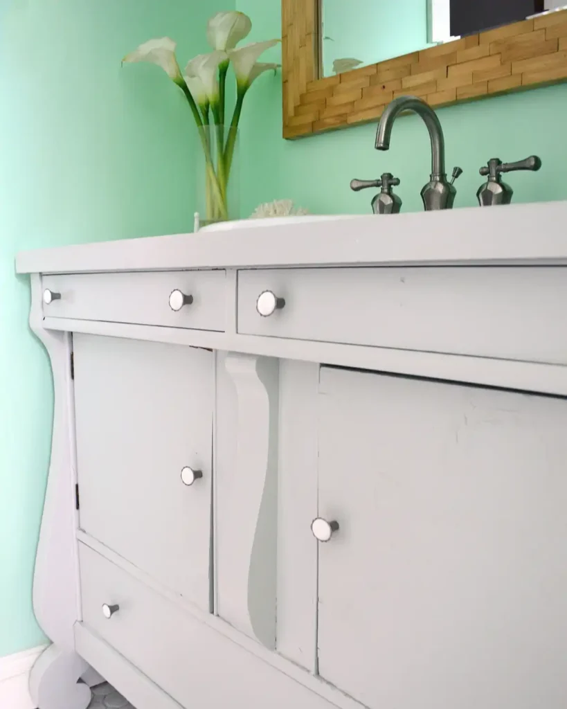 Bathroom vanity wood surface repaired and painted a solid color neutral paint color in a mint colored bathroom with white tiles