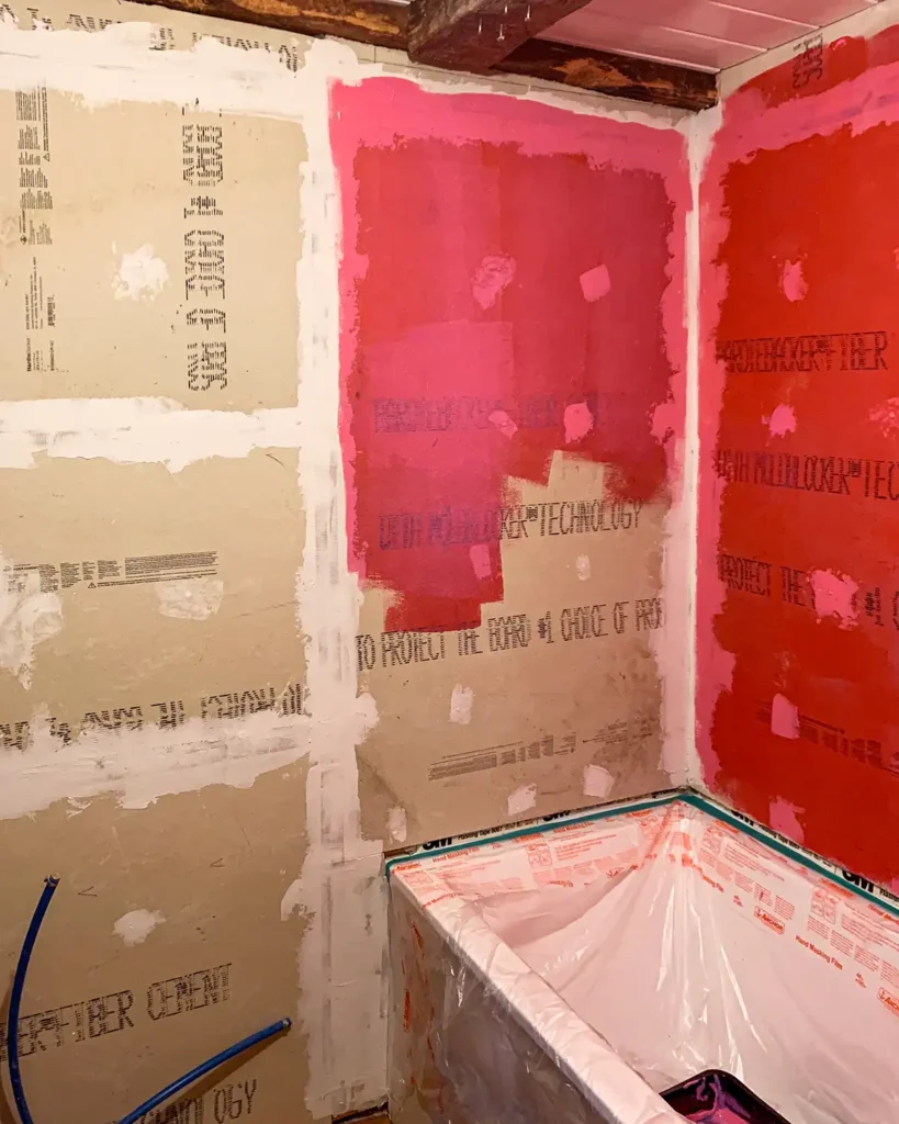 Applying RedGard liquid waterproofing membranes to shower walls using a paint roller, goes on pink but dries red
