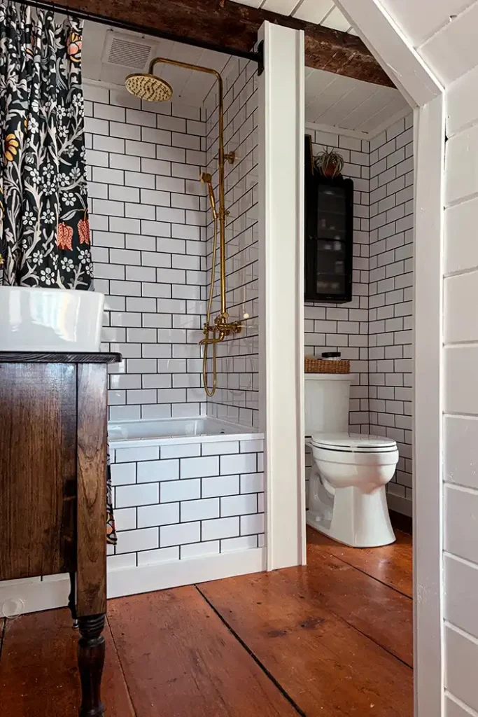 Bathroom renovation DIY featured image with white subway tile, black grout, wide pine floors, and gold shower hardware