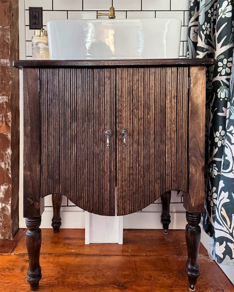 DIY bathroom vanity with reeded trim front, white vessel sink, and white painted wood for a plumbing pipe cover