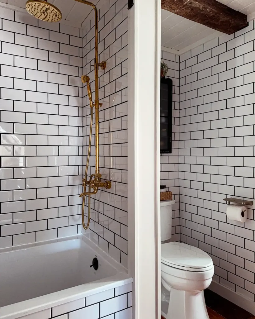 DIY bathroom makeover with wall-to-wall, floor-to-ceiling white subway tile with black grout, toilet nook, and gold shower hardware