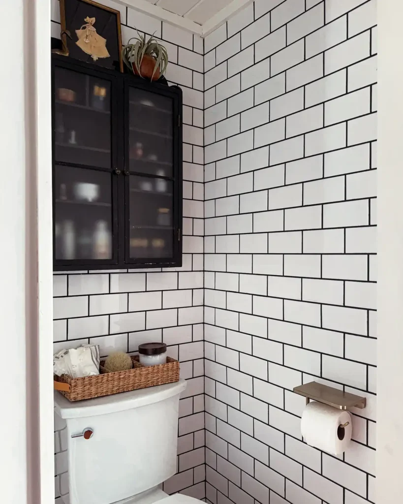 DIY bathroom makeover toilet nook with a toilet tank basket, gold toilet paper holder with shelf, and vintage black cabinet for bathroom storage and organization