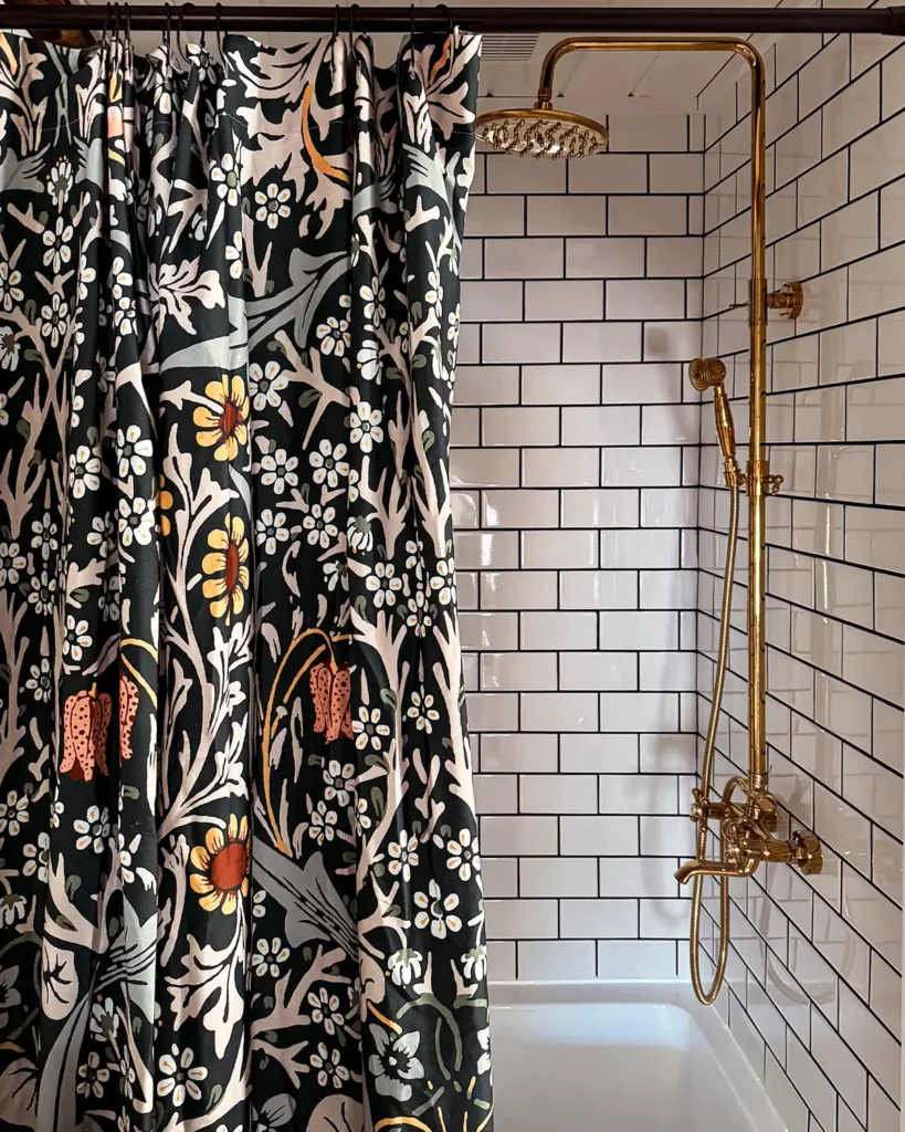 Gold exposed shower hardware with rainfall shower, dark floral shower curtain, white subway tile shower