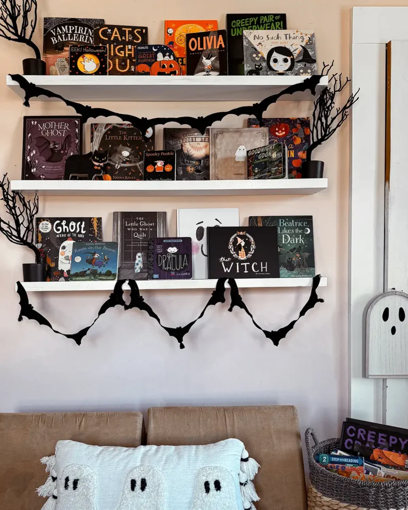 Halloween bookshelves in a kids room with a variety of Halloween books, decorated for Halloween with spooky trees and felt bat garland