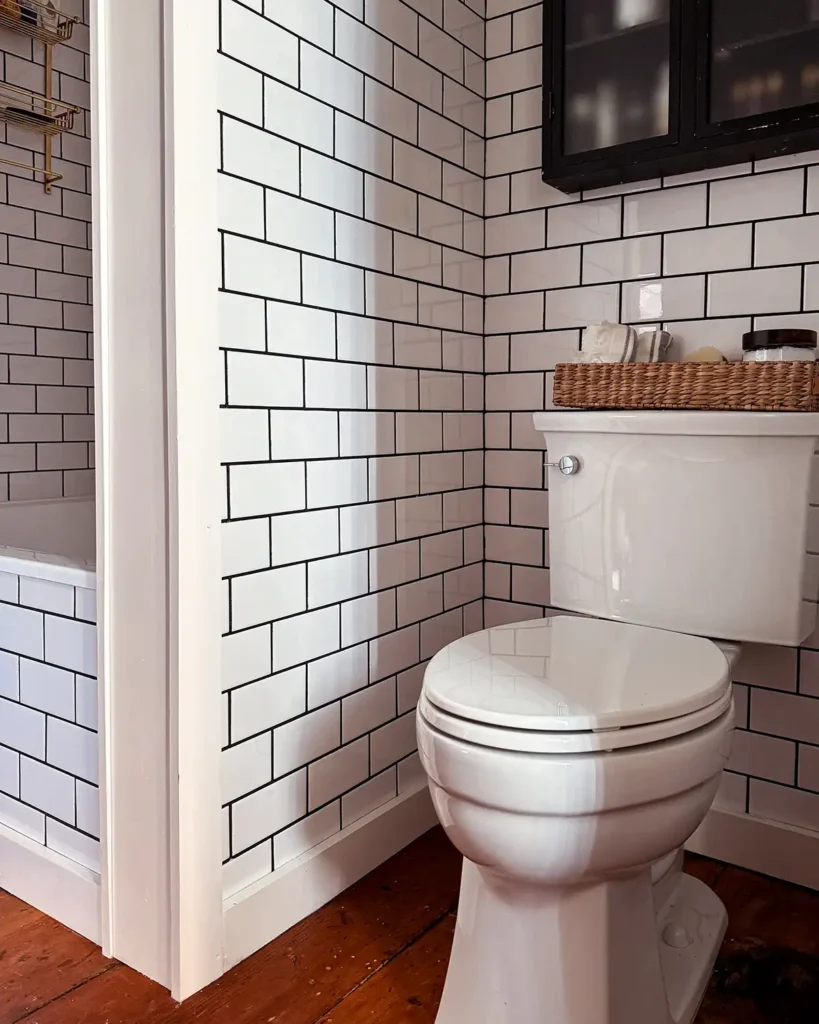 Kohler Elmbrook toilet used in a small bathroom renovation, tucked into a toilet nook, white subway tile bathroom walls with black grout