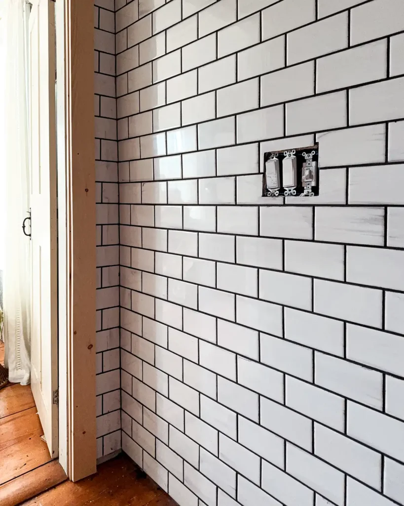 White subway tile wall with a black grout haze that needs to be cleaned, pine trim getting installed around bathroom door opening